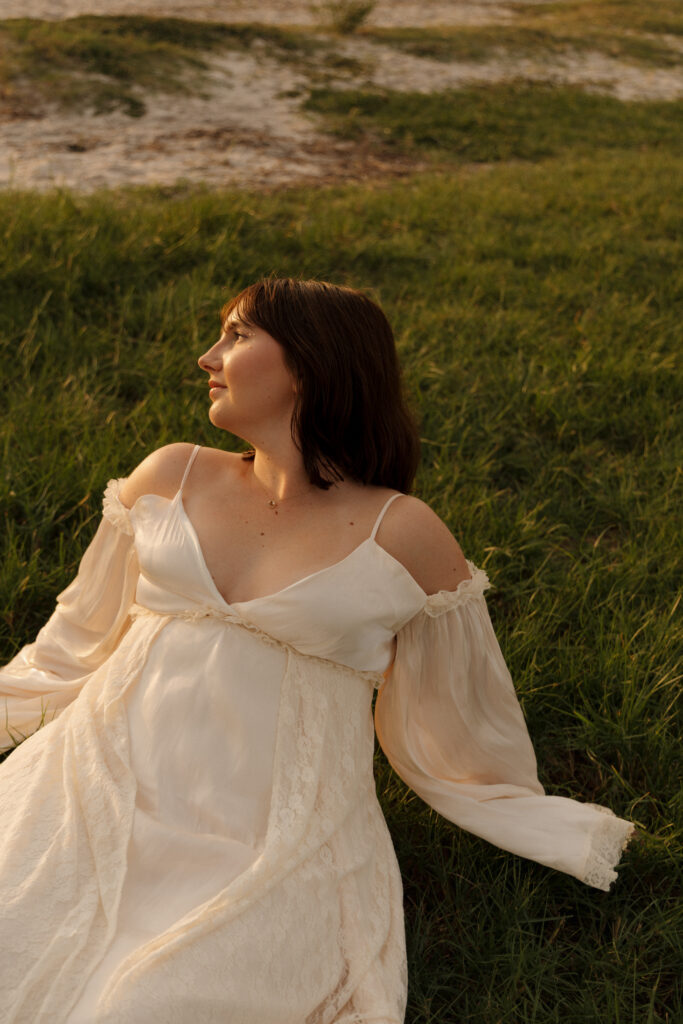 Woman sitting in the grass wearing a flowing white dress during a creative portrait session at Fort Island Gulf Beach