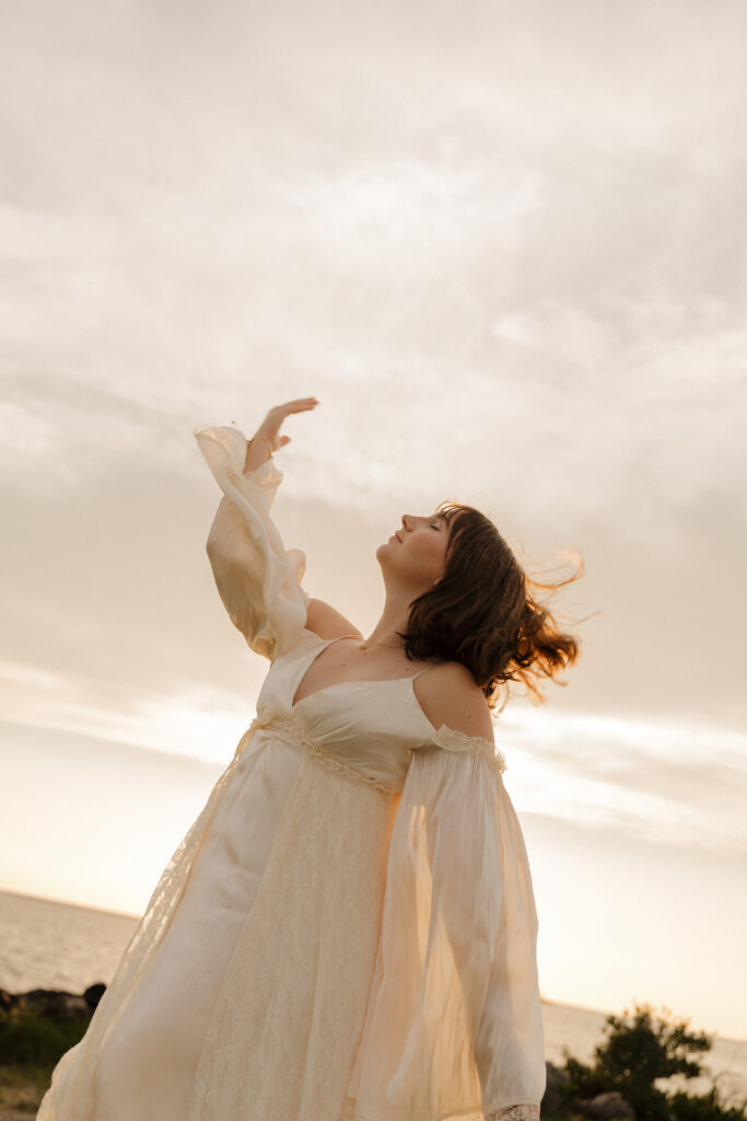Woman moving her arm through the air as her hair blows in the wind during a sunset beach portrait session