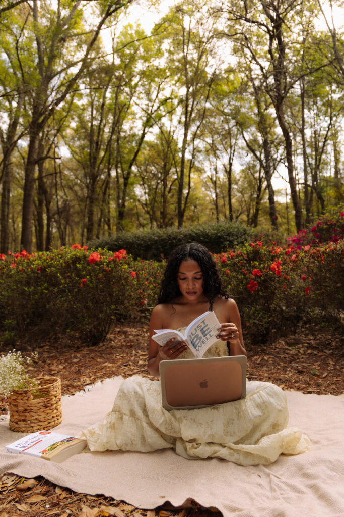 Holistic nurse sitting on a picnic blanket with a laptop and wellness book during an Ocala branding session