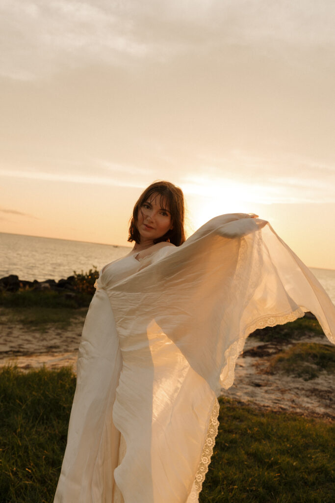 Woman holding out the fabric of her white dress during a creative sunset portrait session in Crystal River Florida