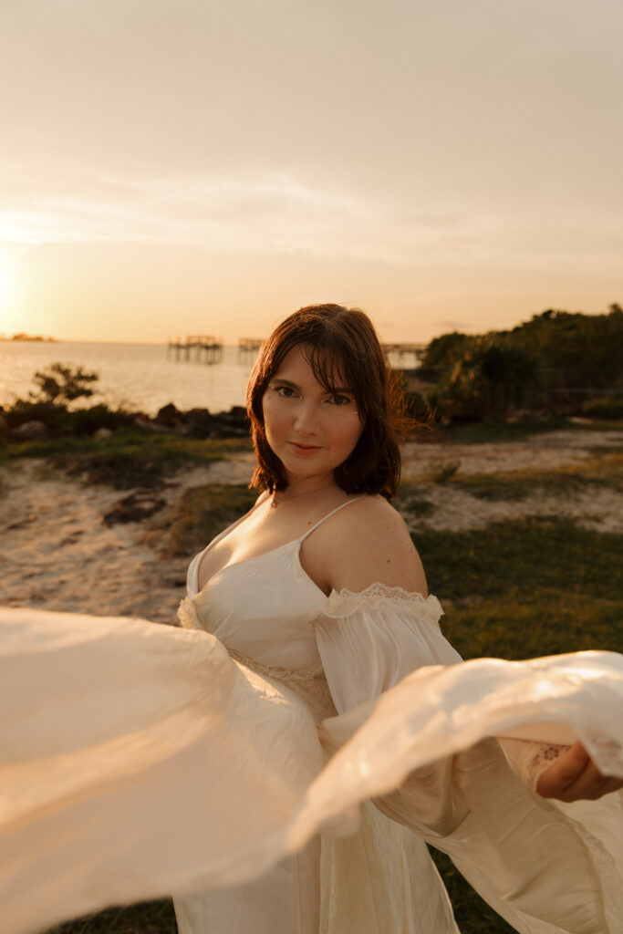 Woman holding the fabric of her dress toward the camera during a creative beach portrait session