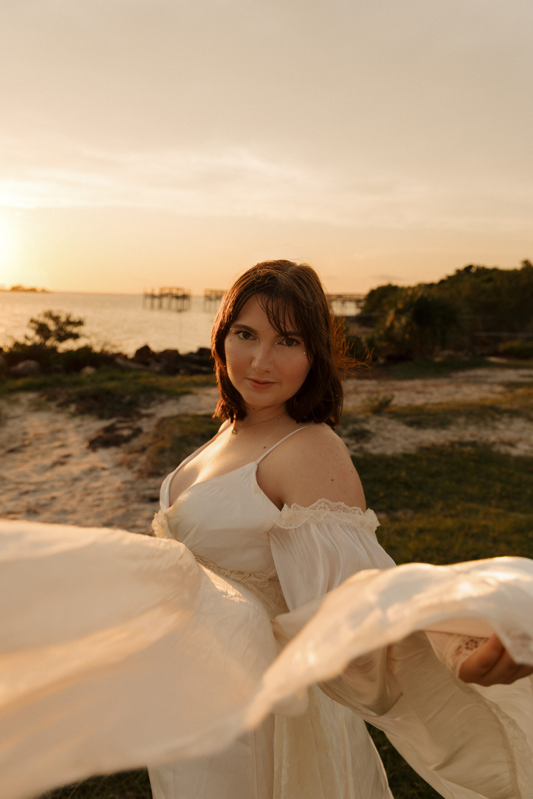 Woman moving her arm through the air as her hair blows in the wind during a sunset beach portrait session