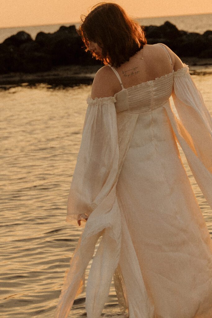 Woman walking through the water in a flowing white dress during golden hour at Fort Island Gulf Beach