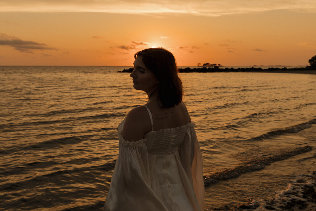 Woman standing along the shoreline silhouetted against the sunset at Fort Island Gulf Beach