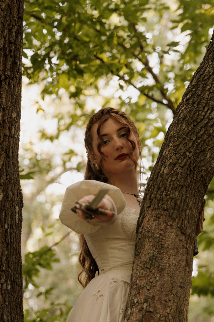 Woman leaning from behind a tree holding an ornate mirror during a creative fantasy portrait session
