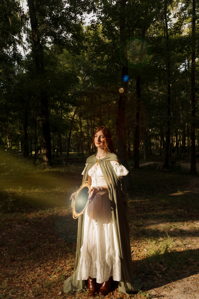 Woman holding an ornate mirror beside a tree during a medieval inspired portrait session in Ocala Florida