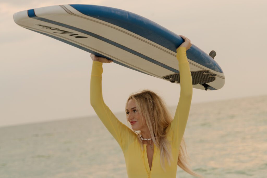 Woman lifting a blue and white Wavestorm surfboard above her head during a surfer inspired portrait session at Sand Key Park in Clearwater Florida