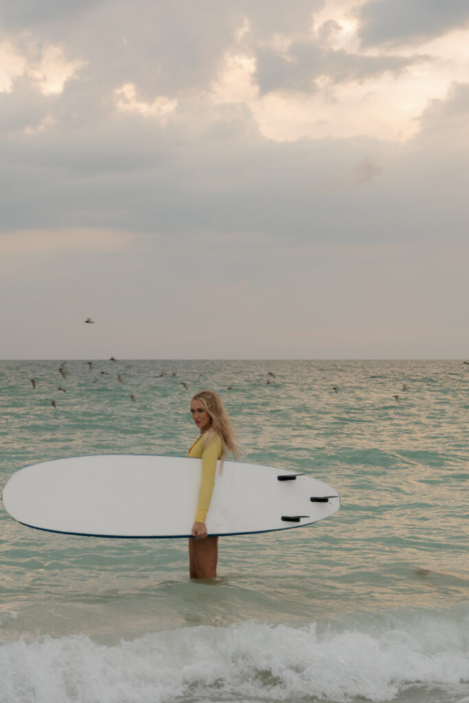 Woman holding a surfboard while standing in shallow water at Sand Key Park in Clearwater Florida