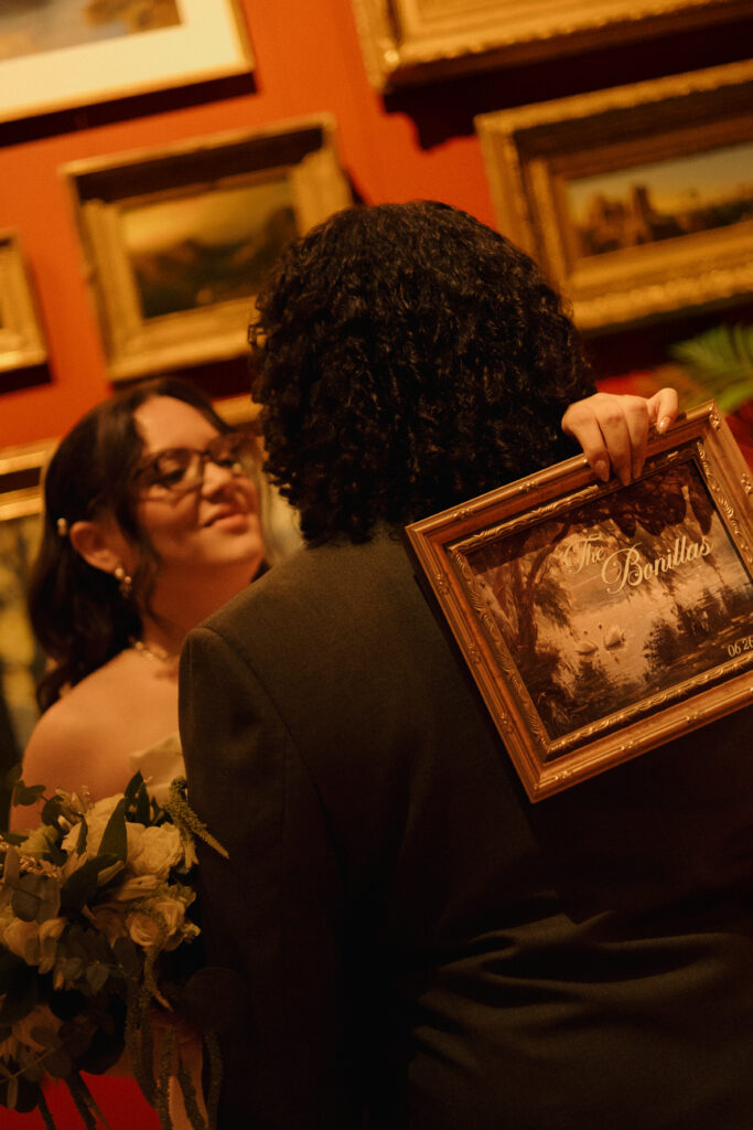 Bride and groom holding a framed Bonillas wedding sign inside the Morse Museum