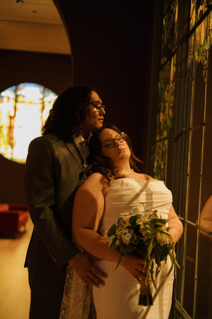 Bride and groom standing beside colorful stained glass during their Morse Museum elopement