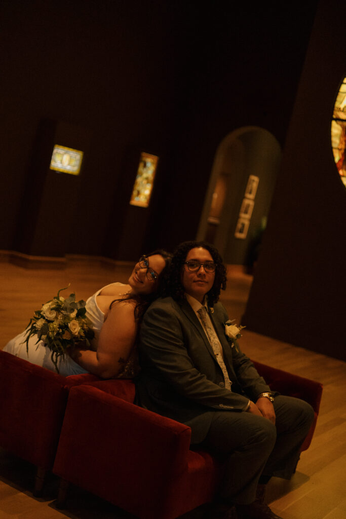 Bride leaning against the groom in red chairs inside the Morse Museum in Winter Park