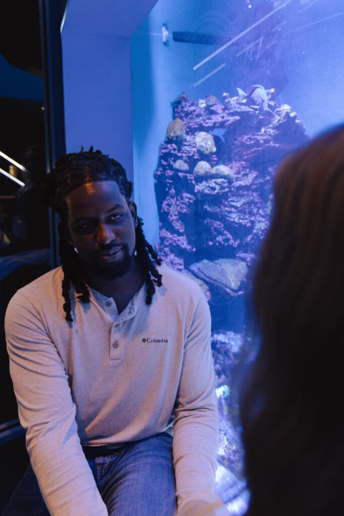 The couple stands together in front of a glowing aquarium tank.